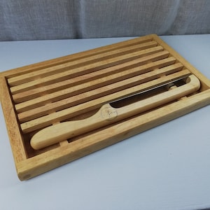 May include: A wooden bread board with a built-in knife holder. The board has a grooved surface and is made of light brown wood.