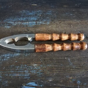 May include: A silver nutcracker with wooden handles. The handles are brown and have a textured surface. The nutcracker is on a dark wooden surface.