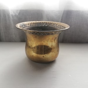 May include: A small, brass planter with a decorative, scalloped rim. The planter is empty and has a shiny, polished finish.