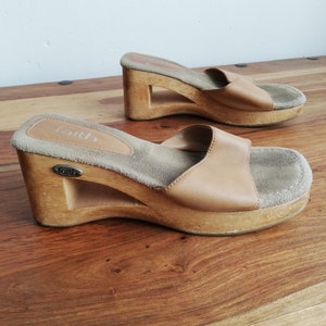 May include: Two pairs of brown leather platform sandals with wooden soles. The sandals have a suede insole and the brand name "Faith" is printed on the insole.