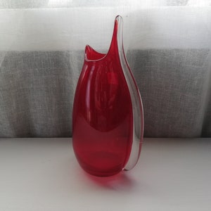 May include: A red glass vase with a clear glass design. The vase has a unique, asymmetrical shape.