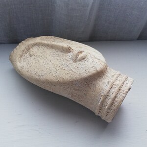 May include: A white ceramic sculpture of a face with a textured surface.