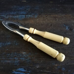 May include: A silver nutcracker with two wooden handles. The nutcracker is on a dark wooden surface.