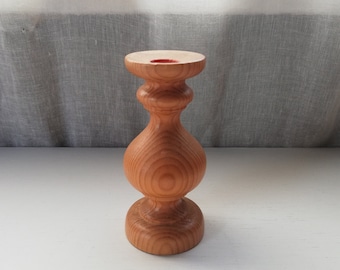 May include: A wooden candle holder with a natural wood finish. The holder has a round base and a cylindrical body with a flared top. The top of the holder has a small, round opening for a candle.