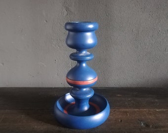 May include: A blue ceramic candle holder with a red band around the middle. The holder has a wide base and a narrow top.