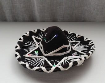 May include: A small black sombrero with white trim and colorful sequins.