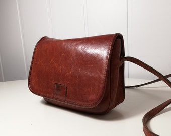 May include: A brown leather crossbody bag with a flap closure and a long adjustable strap.