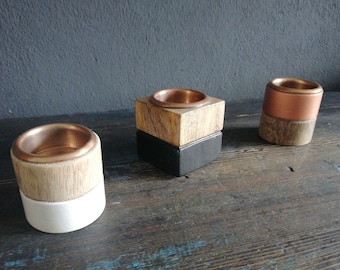 May include: Three wooden candle holders with copper tops. The candle holders are in different shapes and sizes. The candle holders are on a dark wooden surface.