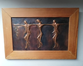 May include: A framed copper wall art piece depicting three stylised figures in a dance-like pose. The figures are raised from the copper background and have a dark patina.