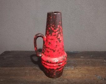 May include: A red and brown ceramic vase with a speckled glaze and a handle. The vase has a rounded base and a narrow neck.