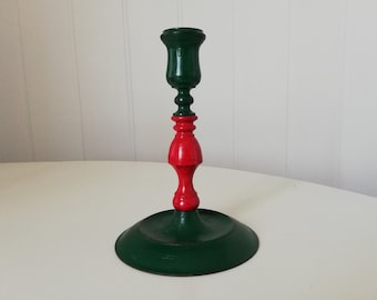 May include: A green and red wooden candlestick with a round base. The candlestick is painted in a two-tone color scheme, with the top portion being green and the bottom portion being red.