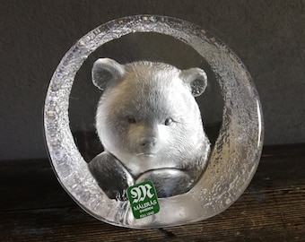 May include: A clear glass paperweight featuring a sculpted panda bear. The paperweight is round with a textured edge. The base of the paperweight has a green label that reads "Maleras Swedish Full Lead".