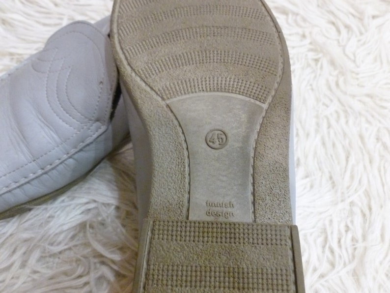 May include: Close-up of the sole of a gray leather shoe with a brown rubber outsole. The shoe size is 45 and the text "Finnish Design" is printed on the sole.