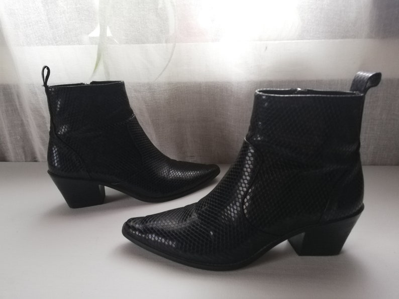 Może przedstawiać: Para czarnych kowbojskich but&oacute;w ze sk&oacute;ry węża z ostrymi noskami i blokowym obcasem.