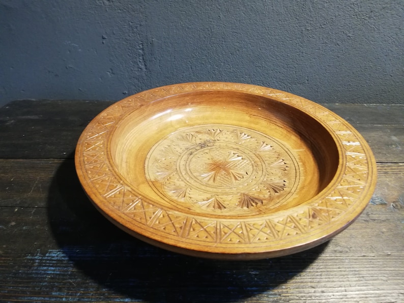 May include: A wooden bowl with intricate carvings in a circular pattern. The bowl is light brown and has a smooth, polished finish.