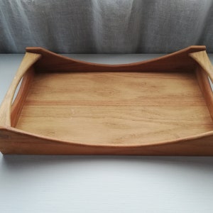 May include: A wooden serving tray with rounded edges and two handles. The tray is made of light brown wood and has a natural finish.