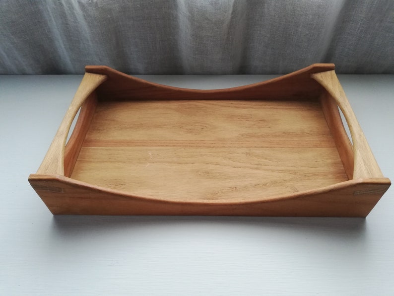 May include: A wooden serving tray with rounded edges and two handles. The tray is made of light brown wood and has a natural finish.