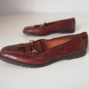 Puede incluir: Un par de mocasines de cuero marr&oacute;n con detalles dorados y borlas. Los mocasines tienen una parte superior de cuero texturizado y una suela de goma negra.