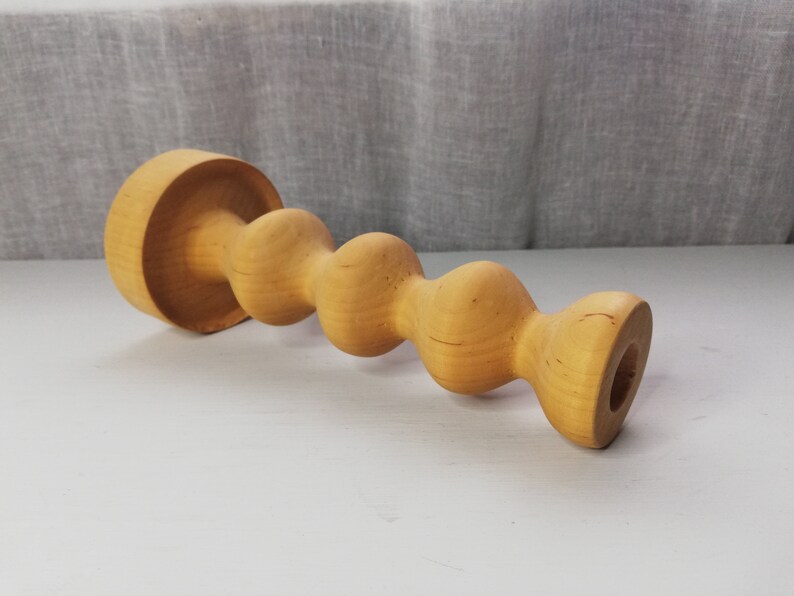 Puede incluir: Un portavelas de madera con un dise&ntilde;o &uacute;nico y retorcido. El portavelas est&aacute; hecho de madera marr&oacute;n claro y tiene un acabado liso y pulido.