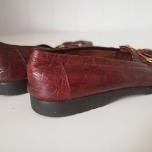 Puede incluir: Un par de mocasines de cuero marr&oacute;n con un detalle de borla y herrajes dorados. Los mocasines tienen un patr&oacute;n texturizado, similar al de un cocodrilo.