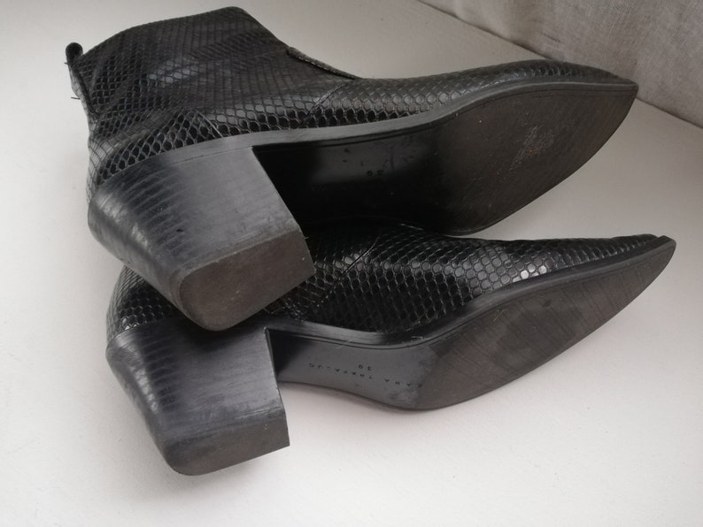 Może przedstawiać: Para czarnych botk&oacute;w z imitacji sk&oacute;ry węża, z ostrym noskiem i grubym obcasem.