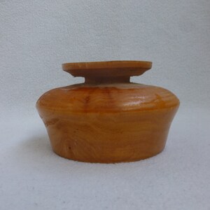 May include: A wooden bowl with a natural wood finish. The bowl has a rounded shape and a slightly raised rim.