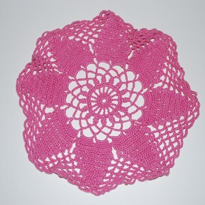 May include: A pink crocheted doily with a delicate floral design.