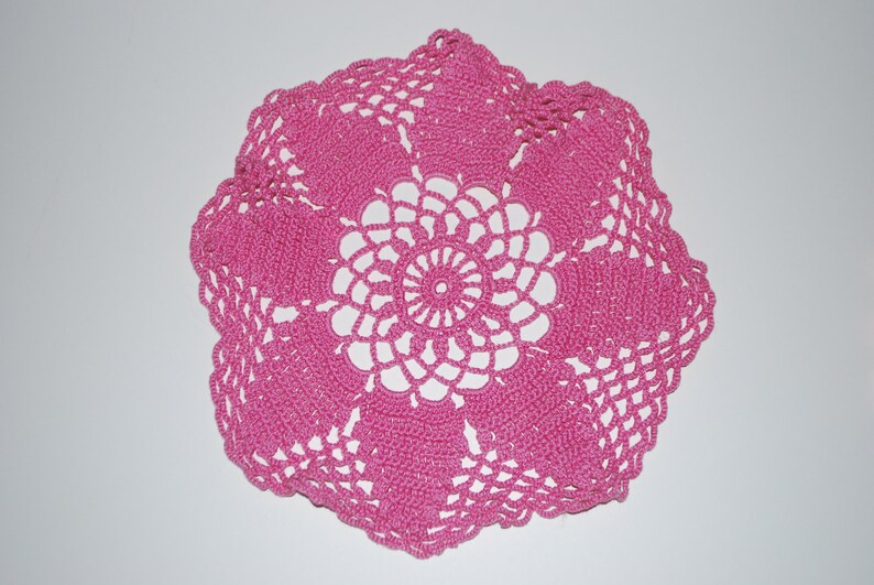 May include: A pink crocheted doily with a delicate floral design.