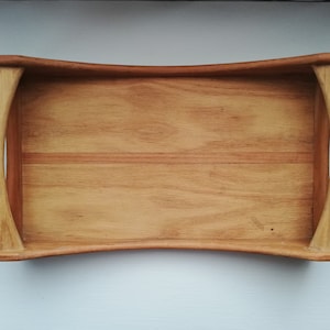 May include: A wooden serving tray with a curved edge and rounded handles. The tray is made of light brown wood with a natural grain pattern.