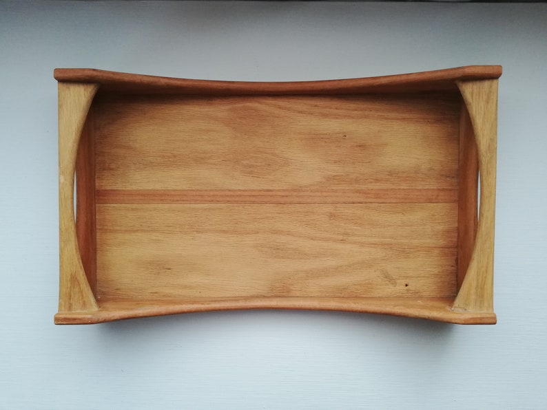 May include: A wooden serving tray with a curved edge and rounded handles. The tray is made of light brown wood with a natural grain pattern.