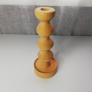 Puede incluir: Un portavelas de madera con un dise&ntilde;o redondeado y bulboso. El portavelas est&aacute; hecho de madera natural y tiene un color marr&oacute;n claro.