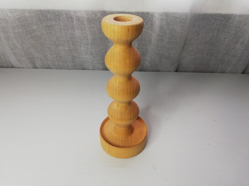 Puede incluir: Un portavelas de madera con un dise&ntilde;o redondeado y bulboso. El portavelas est&aacute; hecho de madera natural y tiene un color marr&oacute;n claro.