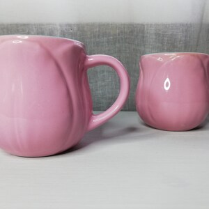 May include: Two pink ceramic mugs with a tulip-shaped design. The mugs have a glossy finish and are perfect for a hot beverage.