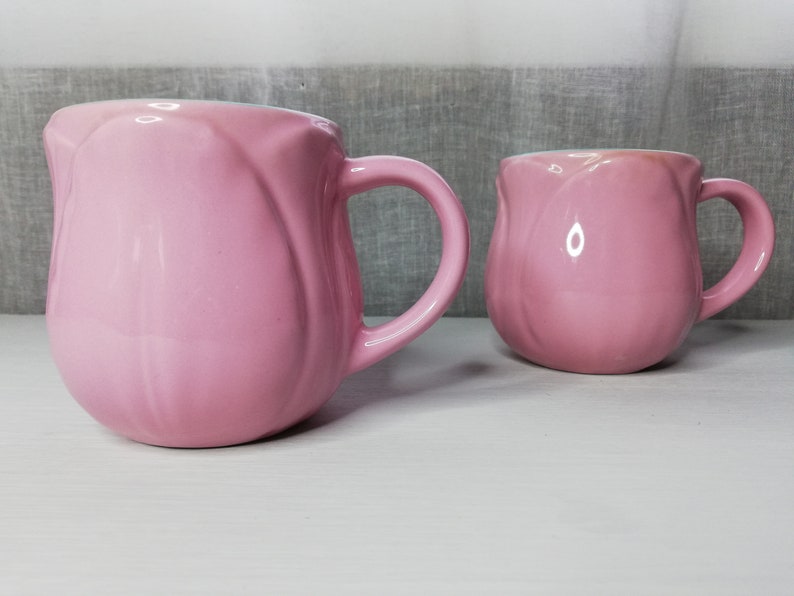 May include: Two pink ceramic mugs with a tulip-shaped design. The mugs have a glossy finish and are perfect for a hot beverage.