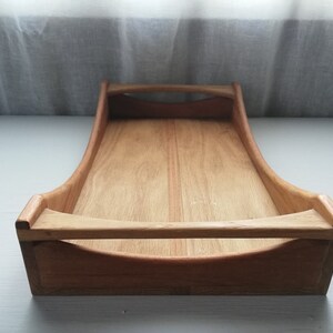 May include: A wooden serving tray with two handles. The tray is made of light brown wood and has a rectangular shape.