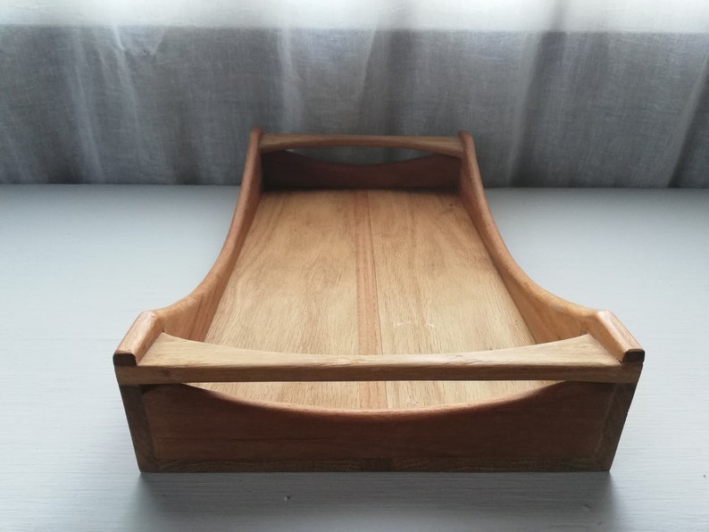 May include: A wooden serving tray with two handles. The tray is made of light brown wood and has a rectangular shape.