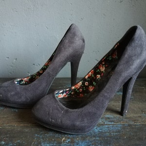 Op de afbeelding: Een paar zwarte su&egrave;de pumps met hoge hakken en een bloemenprint voering.