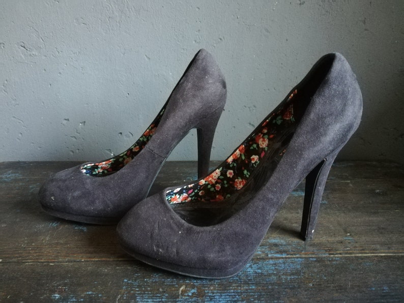 Op de afbeelding: Een paar zwarte su&egrave;de pumps met hoge hakken en een bloemenprint voering.