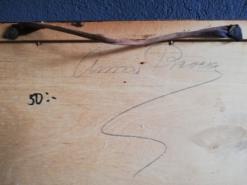 May include: A close-up of the back of a wooden frame with a handwritten signature that reads "Anna Proera" and the number "50" written below. The frame has a brown leather strap attached to it.