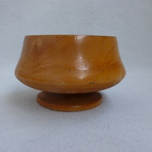 May include: A small, wooden bowl with a flared rim and a pedestal base. The bowl is made of light brown wood and has a smooth, polished finish.
