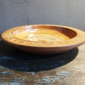 May include: A round wooden bowl with a carved design around the rim. The bowl is made of light brown wood and has a natural finish.