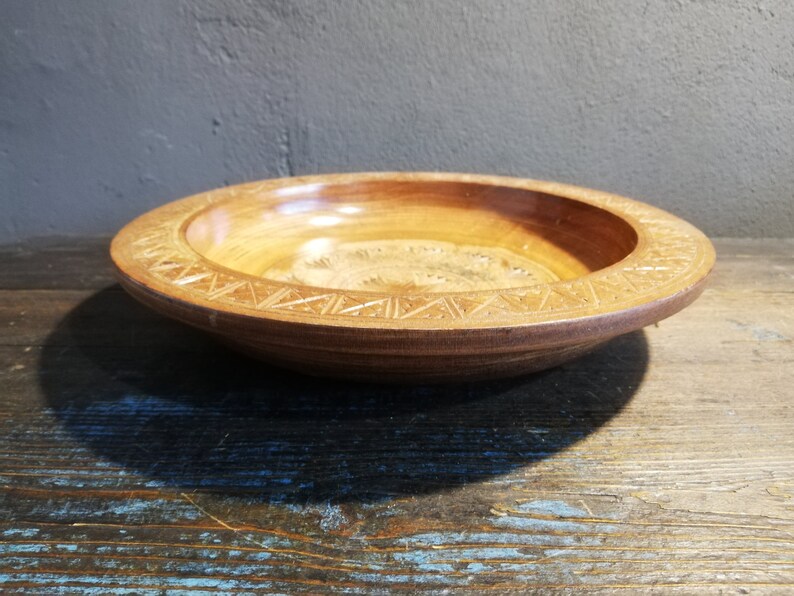 May include: A round wooden bowl with a carved design around the rim. The bowl is made of light brown wood and has a natural finish.