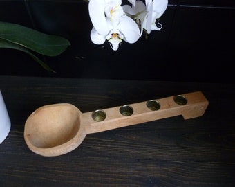 May include: Wooden candle holder with a spoon-shaped handle and four brass candle cups. The holder is made of light brown wood and has a natural finish.