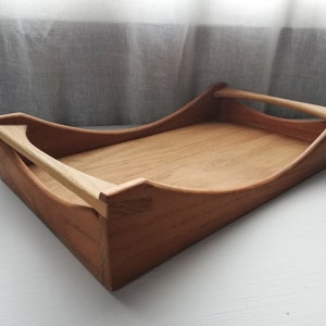 May include: A wooden serving tray with two handles. The tray is made of light brown wood and has a curved shape.