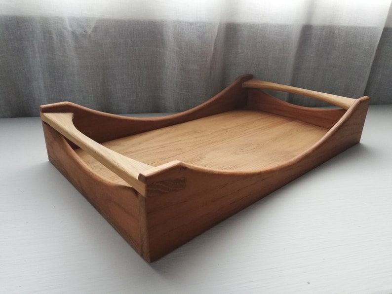 May include: A wooden serving tray with two handles. The tray is made of light brown wood and has a curved shape.