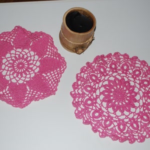 May include: Two pink crocheted doilies with intricate floral patterns.