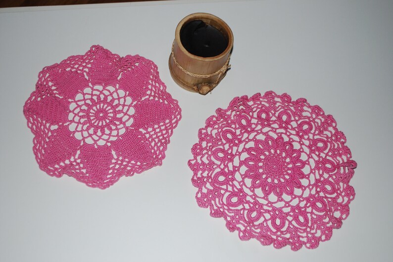 May include: Two pink crocheted doilies with intricate floral patterns.