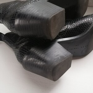 Może przedstawiać: Para czarnych sk&oacute;rzanych kozak&oacute;w ze sk&oacute;ry węża z ostrym noskiem. Kozaki mają gruby obcas i zamek błyskawiczny po wewnętrznej stronie kostki.