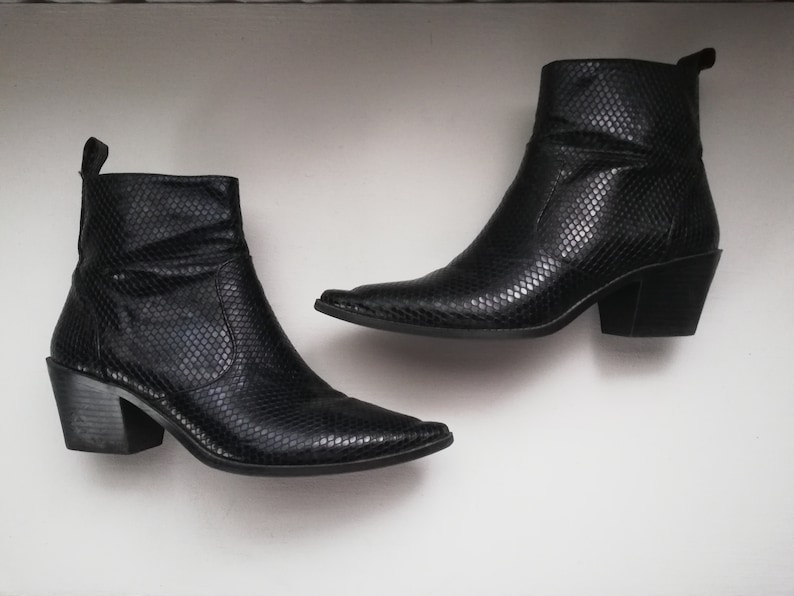 Może przedstawiać: Para czarnych kowbojskich but&oacute;w ze sk&oacute;ry wężowej z ostrymi noskami i blokowym obcasem.