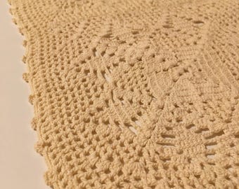 May include: A crocheted oval doily in a cream color with a detailed pattern.